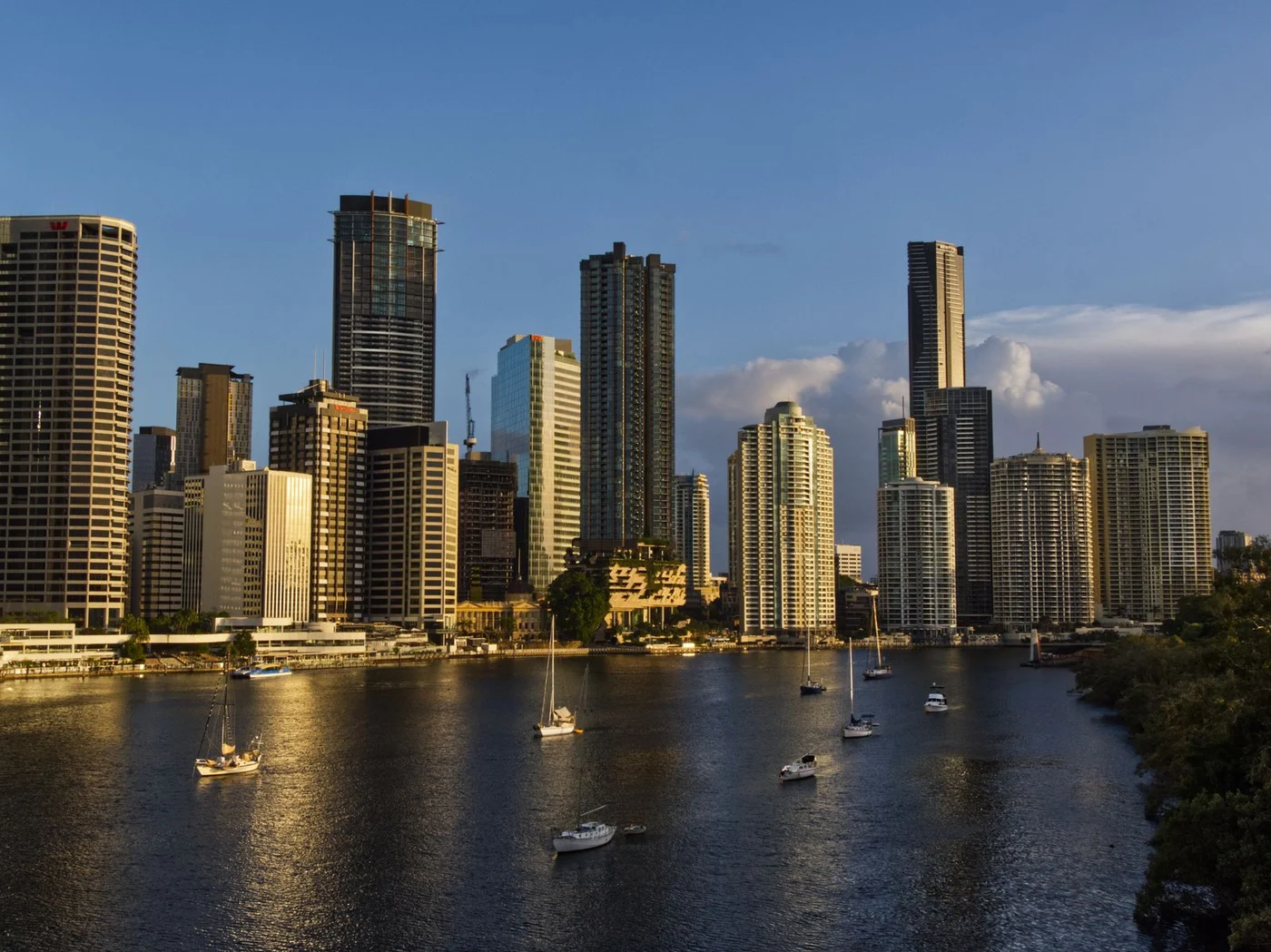 Brisbane riverfront skyline in warm evening light, with boats on the Brisbane River